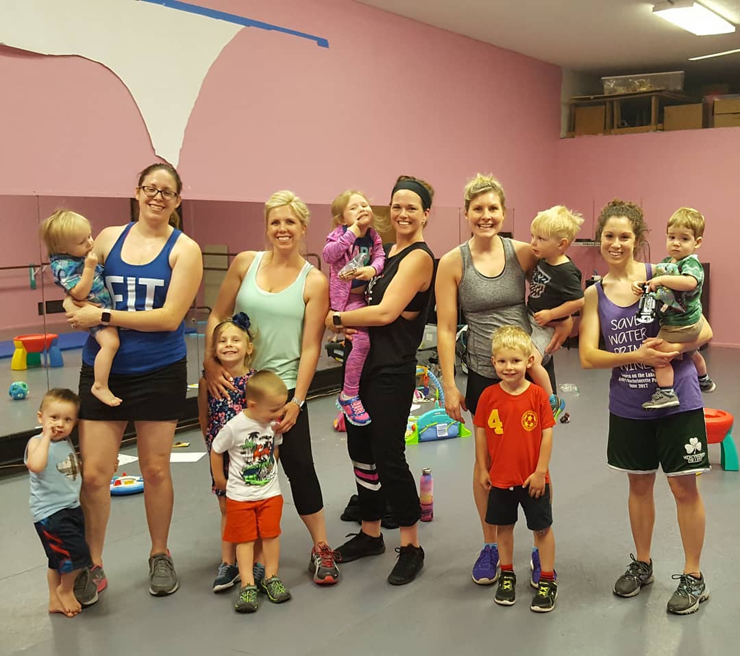 a group of moms working out with their kids at a gym