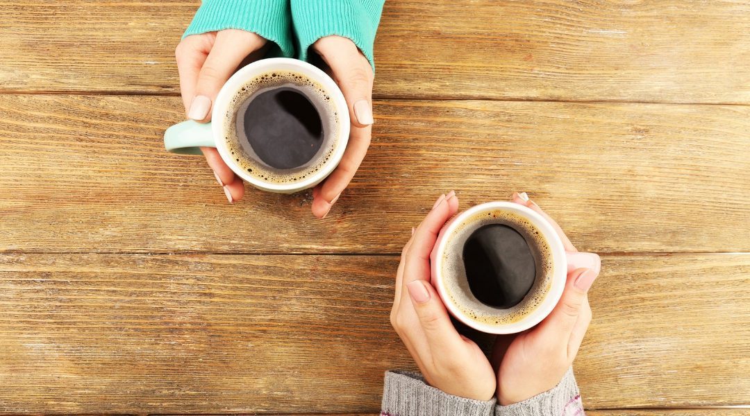 two cups of coffee being sat on a table held by hands