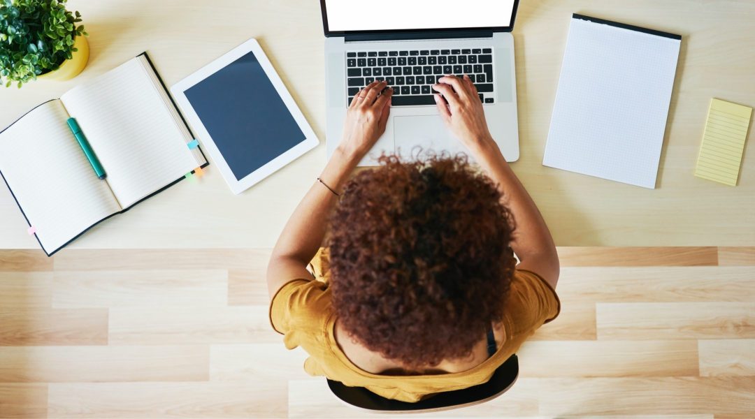 a woman typing on her computer with pads of paper round her desk