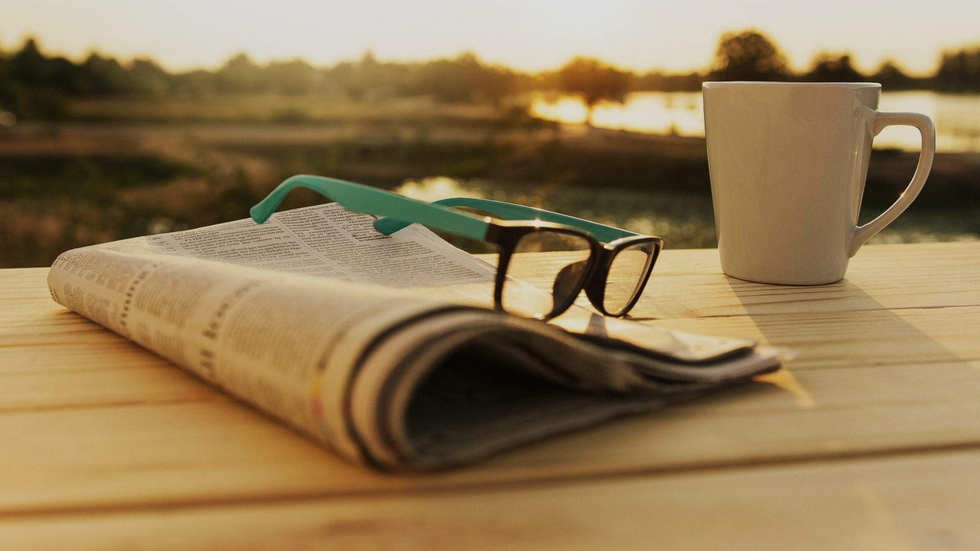 a pair of glasses on a newspaper outside with a cup of coffee watching the sunrise