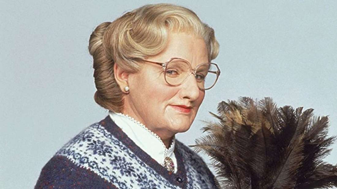 Mrs. Doubtfire wearing eye glasses and holding a feather duster