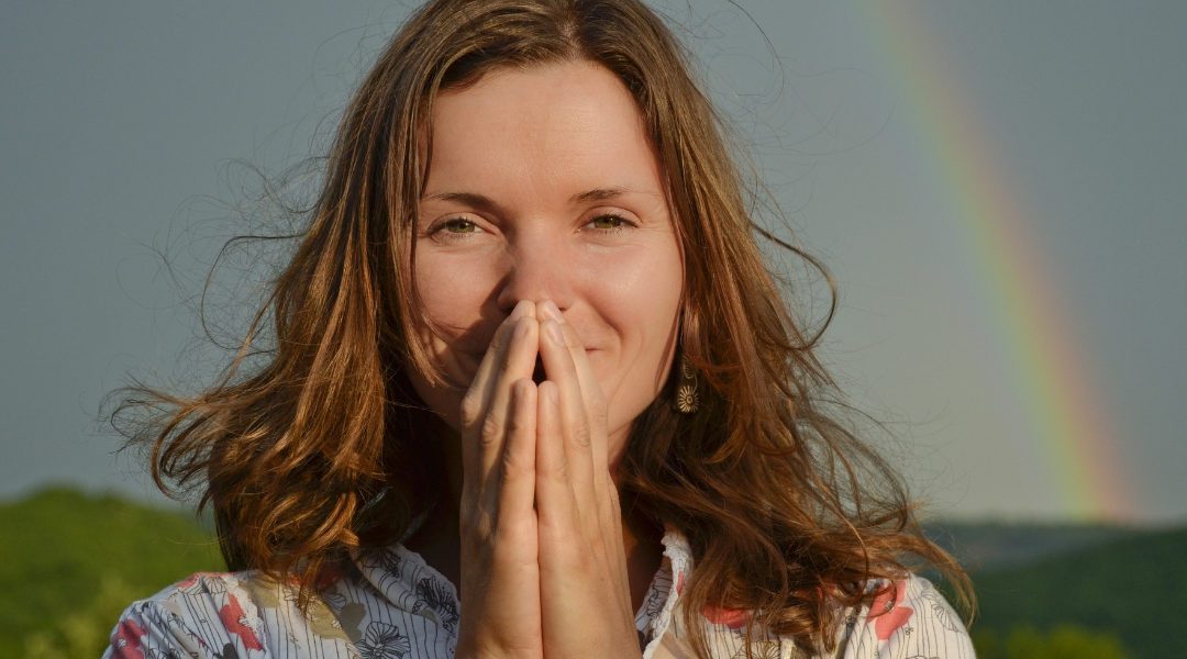 woman in a field with a rainbow in the sky smiling