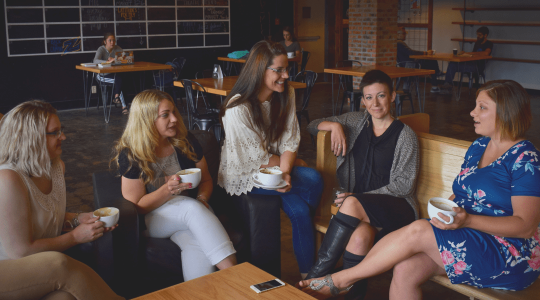 five women in a coffee shop chatting and drinking coffee