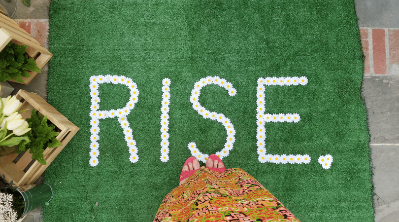 Green turf carpet with the word rise spelled out in daisies
